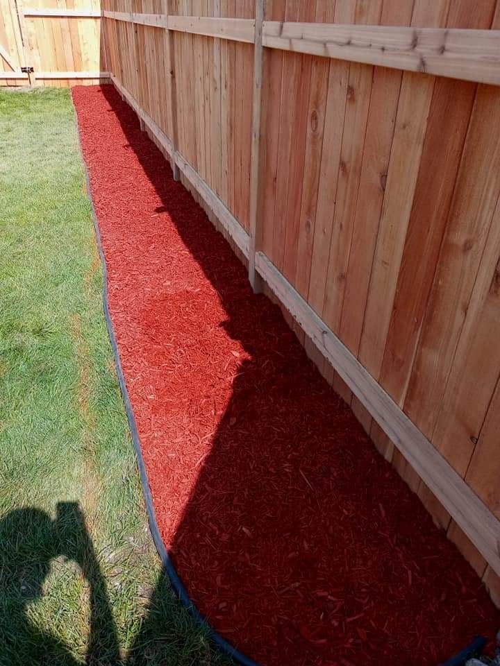 Un macizo largo de mantillo rojo teñido a todo lo largo de una cerca nueva de cedro, contenido con borde negro contra el césped verde