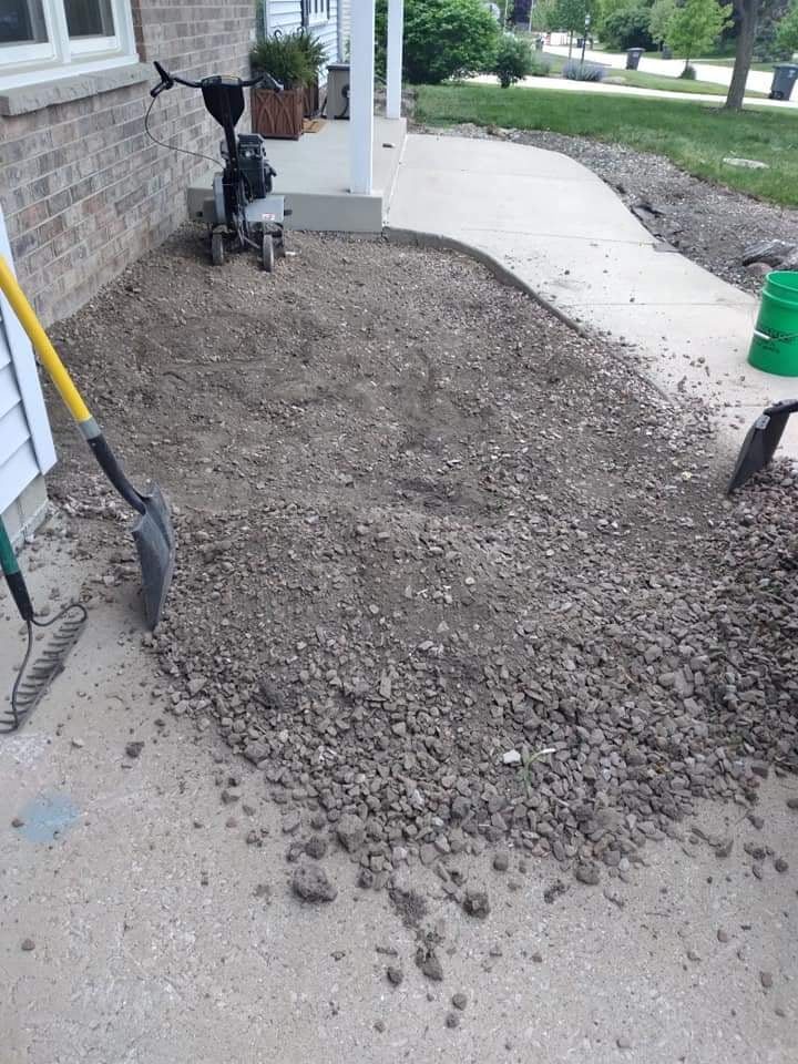El macizo siendo removido y despejado antes de replantar, con motocultor, pala y rastrillo junto a una casa de ladrillo