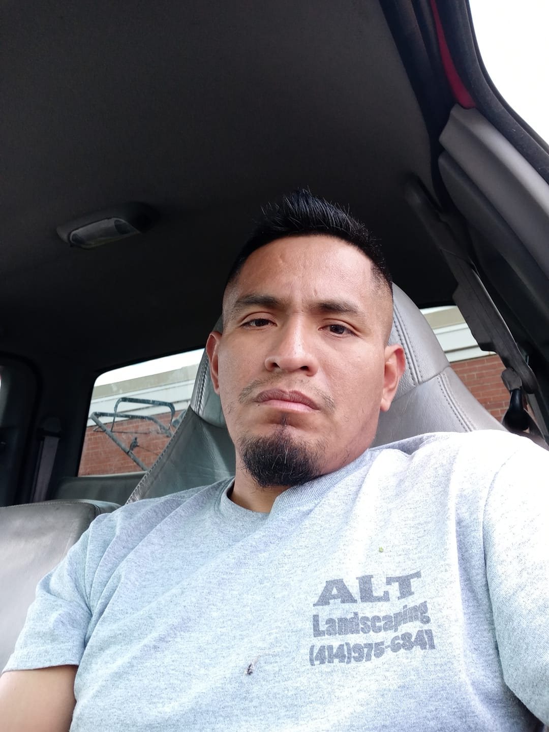 Adolfo Téllez con camisa de trabajo de ALT Landscaping, en su camioneta entre trabajos